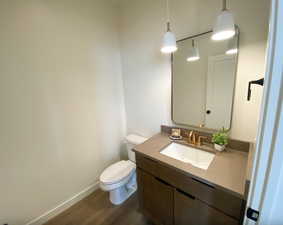 Half bathroom featuring toilet, vanity, wood finished floors, and baseboards
