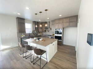 Kitchen featuring light wood finished floors, backsplash, a sink, wall chimney exhaust hood, and appliances with stainless steel finishes