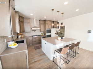 Kitchen with wall chimney range hood, decorative backsplash, appliances with stainless steel finishes, and light wood-type flooring