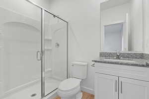 Full bathroom featuring a stall shower, toilet, baseboards, wood finished floors, and vanity