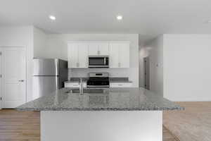 Kitchen featuring dark stone counters, a sink, an island with sink, white cabinetry, and appliances with stainless steel finishes