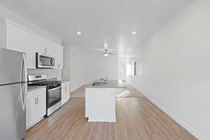 Kitchen featuring ceiling fan, stainless steel appliances, a center island with sink, light wood finished floors, and white cabinets