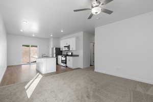 Kitchen with stainless steel appliances, a kitchen island with sink, baseboards, white cabinetry, and a ceiling fan