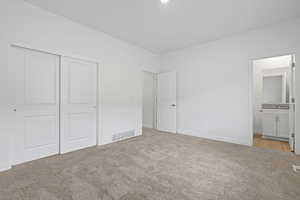 Unfurnished bedroom featuring ensuite bathroom, baseboards, visible vents, light colored carpet, and a closet
