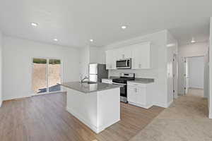 Kitchen featuring stainless steel appliances, a sink, baseboards, a center island with sink, and white cabinetry