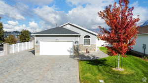 Ranch-style house featuring fence, stone siding, and a garage