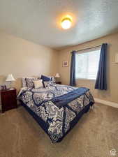 Bedroom with a textured ceiling, carpet flooring, and baseboards
