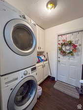 Clothes washing area with dark wood-style floors, cabinet space, stacked washing maching and dryer, and a textured ceiling