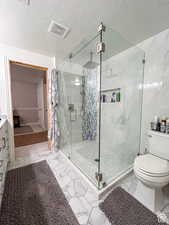 Bathroom with a shower stall, a textured ceiling, marble finish floor, toilet, and visible vents