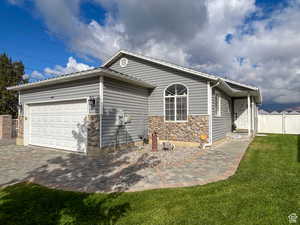 View of property exterior featuring fence, driveway, stone siding, a lawn, and a garage