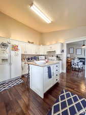 Kitchen featuring white cabinets, under cabinet range hood, light countertops, white appliances, and dark wood-type flooring