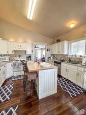 Kitchen with vaulted ceiling, a textured ceiling, under cabinet range hood, and white appliances