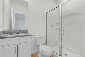 Bathroom featuring a shower stall, wood finished floors, vanity, baseboards, and toilet