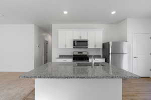 Kitchen featuring dark stone counters, a sink, an island with sink, white cabinetry, and appliances with stainless steel finishes