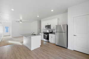 Kitchen featuring a sink, stainless steel appliances, a center island with sink, light wood-style flooring, and white cabinets