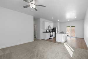 Kitchen with a kitchen island with sink, appliances with stainless steel finishes, baseboards, white cabinetry, and recessed lighting