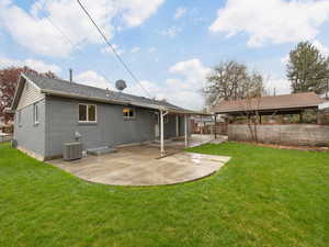 Back of house with central AC unit, fence, brick siding, a lawn, and a patio
