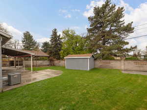 View of yard featuring central AC, a patio area, a fenced backyard, an outbuilding, and a storage unit