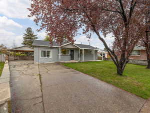 Ranch-style house with covered porch, concrete driveway, brick siding, fence, and a front yard