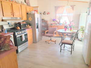 Kitchen with under cabinet range hood, light wood-style floors, light brown cabinets, decorative light fixtures, and appliances with stainless steel finishes