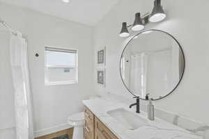 Bathroom featuring a shower with curtain, toilet, baseboards, wood finished floors, and vanity
