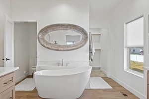 Owner's Suite Bathroom featuring wood finished floors, visible vents, vanity, baseboards, and a soaking tub