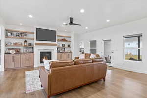 Living room with light wood finished floors, visible vents, a glass covered fireplace, recessed lighting, and a ceiling fan