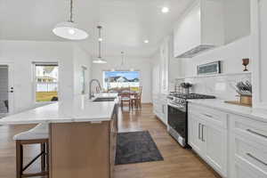 Kitchen featuring a breakfast bar, stainless steel range with gas stovetop, a sink, premium range hood, and light wood-type flooring