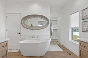 Owner's Suite Bathroom with a soaking tub, visible vents, vanity, and wood finished floors