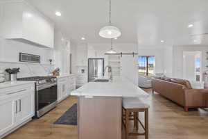Kitchen featuring white cabinets, open floor plan, decorative backsplash, appliances with stainless steel finishes, and a breakfast bar area