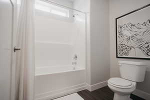 Bathroom with shower / bath combo, wood finished floors, baseboards, and toilet