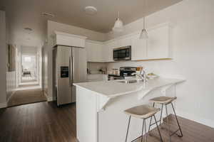 Kitchen featuring stainless steel appliances, a peninsula, a sink, dark wood-style flooring, and baseboards