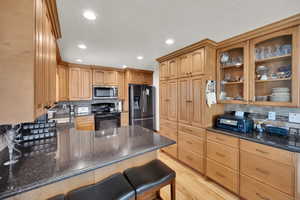 Kitchen featuring a peninsula, stainless steel microwave, tasteful backsplash, black range with electric stovetop, and refrigerator with ice dispenser