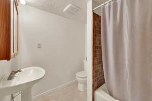Bathroom featuring tile patterned floors, a textured ceiling, toilet, baseboards, and visible vents