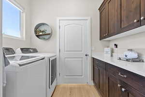 Clothes washing area with separate washer and dryer, light wood-style floors, and cabinet space
