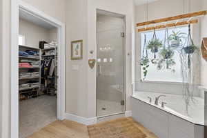 Bathroom featuring a shower stall, wood finished floors, a bath, a walk in closet, and baseboards