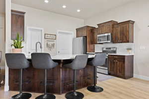 Kitchen with a kitchen breakfast bar, light wood-style flooring, backsplash, light countertops, and appliances with stainless steel finishes