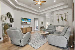 Living area with a tray ceiling, visible vents, recessed lighting, light wood-style floors, and ceiling fan