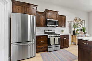 Kitchen with dark brown cabinets, light countertops, light wood-style floors, and appliances with stainless steel finishes