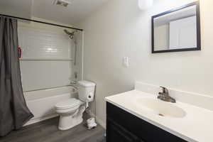 Full bath with wood finished floors, visible vents, toilet, vanity, and shower / tub combo with curtain