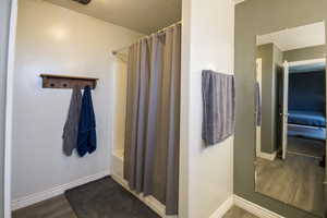 Bathroom with baseboards, shower / tub combo with curtain, wood finished floors, and a textured ceiling