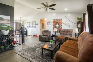 Living area with baseboards, lofted ceiling, wood finished floors, and ceiling fan with notable chandelier