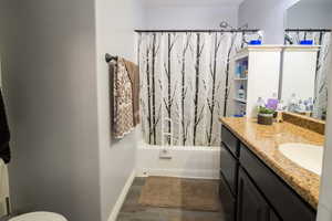 Bathroom with toilet, baseboards, shower / bath combo with shower curtain, wood finished floors, and vanity