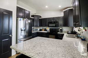 Kitchen featuring a peninsula, a sink, recessed lighting, dark cabinets, and black appliances