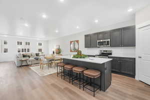 Kitchen featuring a kitchen breakfast bar, light wood-type flooring, stainless steel appliances, light countertops, and a kitchen island