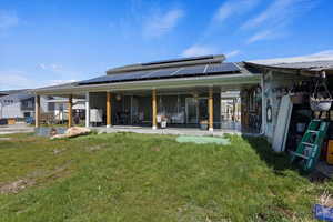 Rear view of house with solar panels, a patio area, and a lawn