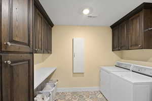 Clothes washing area with washer and dryer, baseboards, cabinet space, and visible vents