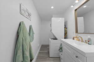 Bathroom featuring baseboards, recessed lighting, wood finished floors, vanity, and stacked washing maching and dryer
