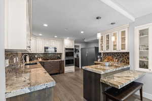 Kitchen featuring dark wood finished floors, stainless steel appliances, a sink, a peninsula, and glass insert cabinets