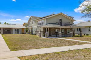 View of front of home featuring an outbuilding, stone siding, covered porch, a balcony, and a front yard